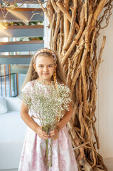 Cute girl, Caucasian, blond hair and pink pastel dress with a bouquet of gypsophila flowers. Modern interior. Spring concept