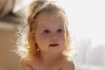 Sweet curly girl sit in bed. Smiling baby girl 2-3 year old. Looking at camera. Childhood. Playful