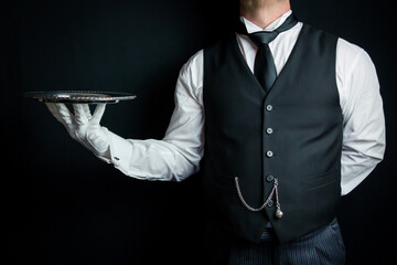 Formal Butler or Waiter in Black Waistcoat and White Gloves Holding Serving Tray Elegantly. Service Industry and Professional Hospitality.