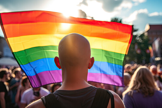 Photo of a man hodling LGBT Flag during pride march with crowd