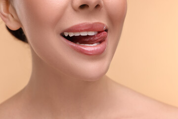 Fototapeta premium Woman with beautiful lips licking her teeth on beige background, closeup