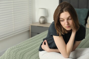Sad young woman sitting on bed at home, space for text