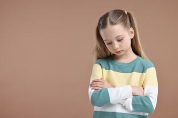 Portrait of sad girl with crossed arms on light brown background, space for text