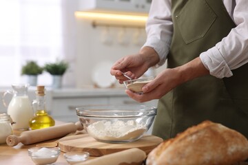 Making bread. Man putting dry yeast into bowl with flour at wooden table in kitchen, closeup