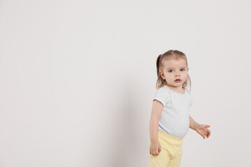 Cute little girl standing near white wall at home, space for text