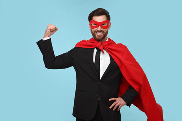 Obraz na płótnie Canvas Businessman wearing red superhero cape and mask on light blue background
