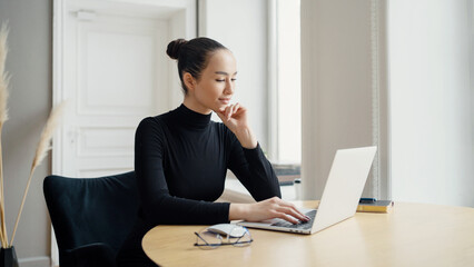Serene young woman using laptop in a bright room, epitome of focused work.