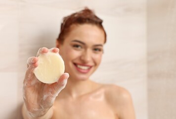 Happy young woman with solid shampoo bar in shower, selective focus. Space for text