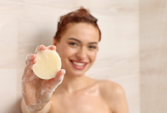 Happy young woman with solid shampoo bar in shower, selective focus. Space for text