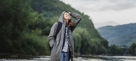 A young woman in a raincoat walking along the bank of a mountain river. Rest travel and relaxation...