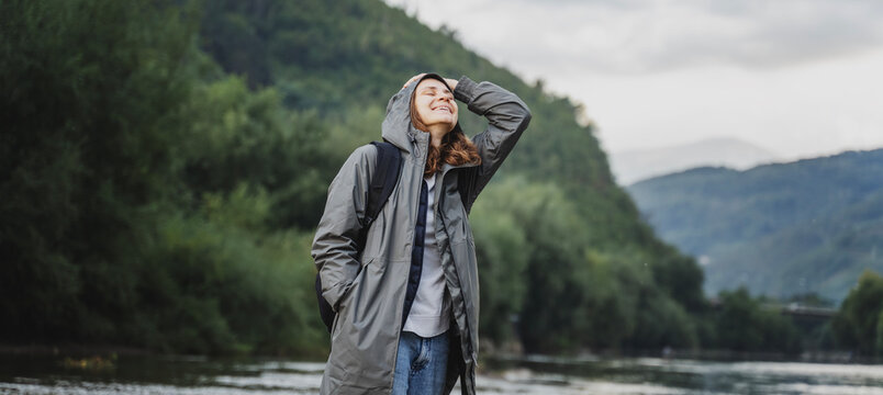 A young woman in a raincoat walking along the bank of a mountain river. Rest travel and relaxation with nature