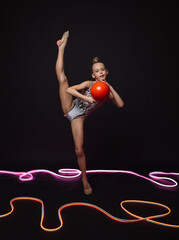 Girl gymnast performs gymnastic elements in the studio on a black background with neons