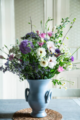 Blumenstrauss in einer Vase aus Keramik vor einer Glastür. Frühlingsblumen: Kamille, Eustoma, Anemone, Spirea, Allium, Strandflieder, Zweige