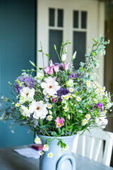 Blumenstrauss in einer Vase aus Keramik vor einer petrolfarbenen Wand. Frühlingsblumen: Kamille, Eustoma, Anemone, Spirea, Allium, Strandflieder, Zweige