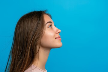 Smiling girl showing advertisement blank area in side profile portrait on vibrant blue background - obrazy, fototapety, plakaty
