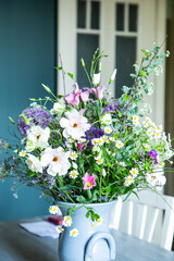 Blumenstrauss in einer Vase aus Keramik vor einer petrolfarbenen Wand. Frühlingsblumen: Kamille, Eustoma, Anemone, Spirea, Allium, Strandflieder, Zweige