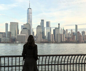 woman looking at downtown manhattan nyc skyline (after sunset, night time)  world trade center cityscape (high rise urban buildings) railing, hudson river, waterfront, bay, harbor new york city view