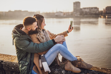 Happy couple photographing  cityscape with mobile phone  while spending time together by the river.
