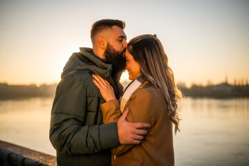 Happy couple enjoy spending time together outdoor on a sunset. Man is kissing his woman in forehead.