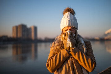 Woman in warm clothing blowing nose outdoor.