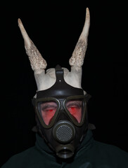 A scary man with glowing red eyes and horns peers through a gas mask, his gaze piercing the...