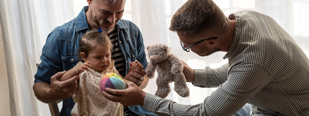 Horizontal banner or header with male gay couple with adopted baby girl at home - Two handsome fathers playing with their daughter - Diversity concept and LGBTQ family relationship