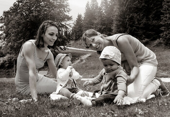 Female lesbian couple with two adopted baby girl during a pic-nic at the park - Two mothers relaxing with the baby girls on lawn - Female babysitters - LGBT family concept - Black and white editing