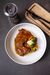 A plate of beef ribs in barbecue sauce with vegetables and mashed potatoes on dark background top view