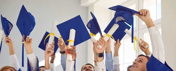 Cropped photo of a group of smiling graduates students standing indoors with hands up holding...