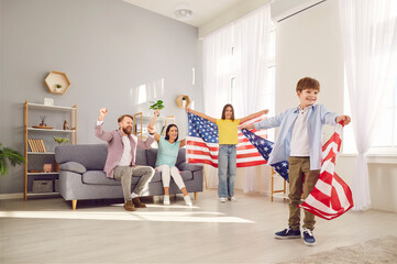 Young excited happy American parents with two children boy and girl sitting at home with flag of united states celebrating Independence Day. Family patriotism and US patriotic holiday concept.