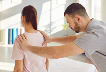 Physiotherapy. Focused male rehabilitation therapist works with female patient performing physical assessment of her shoulder. Doctor palpates woman's shoulder blade in modern rehabilitation facility.