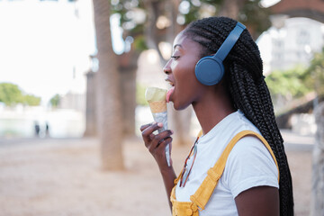 Young woman listening to music and eating ice cream while walking through the city