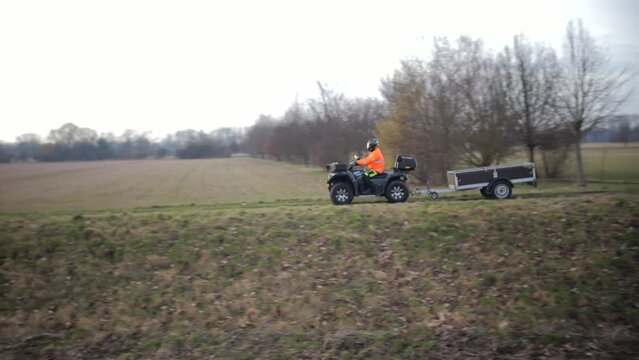 ATV Rider in High Visibility Jacket Towing a Trailer Across a Field