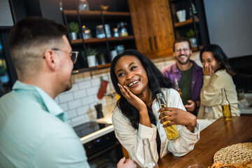 Two diverse young friends laughing together during a dinner together in a friend's kitchen