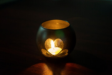A handmade candle holder. A candle holder made of a glass jar, in the shape of a heart, stands on a table in a dark room. Valentine's Day, decoration, romantic atmosphere - Powered by Adobe