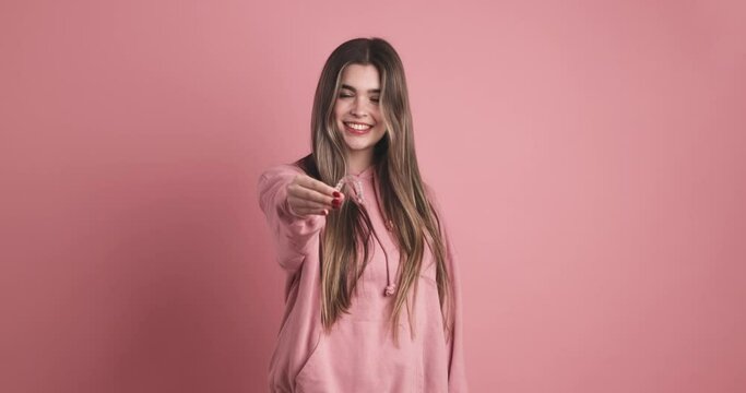 Happy woman showing dental clear aligner in pink studio