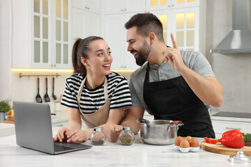 Fototapeta na wymiar Happy lovely couple using laptop while cooking in kitchen