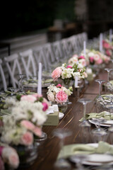 A large, long, decorated, wooden table and chairs, covered with a white tablecloth with dishes, flowers, candles.