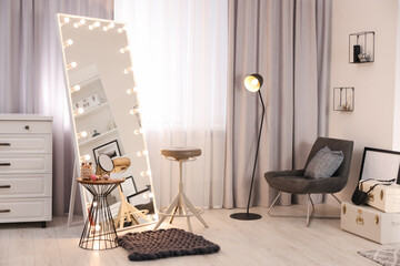 Makeup room. Stylish mirror with light bulbs, beauty products on table and chair indoors