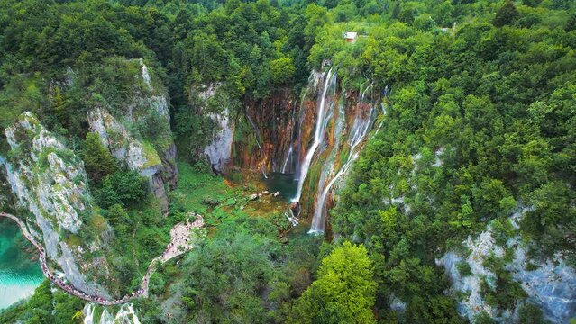 Spring high waterfall cascading over lush green cliff in dense summer forest. Mountain lake with clear water.