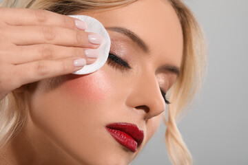 Obraz na płótnie Canvas Beautiful woman removing makeup with cotton pad on light grey background, closeup