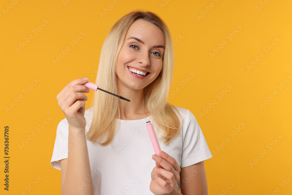 Wall mural Beautiful woman with mascara on orange background