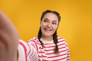 Smiling woman with braces taking selfie on orange background