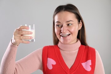 Happy woman with milk mustache holding glass of drink on light grey background