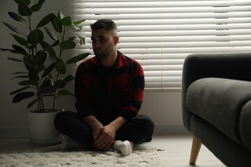 Fototapeta premium Sad man sitting near closed blinds indoors
