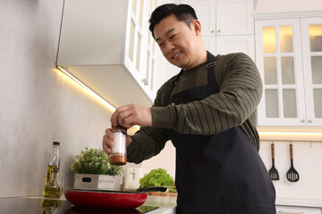Cooking process. Man adding salt into frying pan in kitchen, low angle view