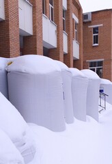 Large bags of expanded clay stand near a brick building and are covered with snow