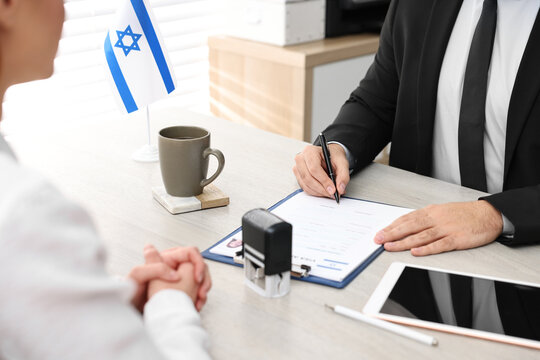 Immigration to Israel. Embassy worker signing application form at wooden table, closeup