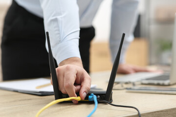 Man inserting cable into Wi-Fi router at wooden table indoors, closeup - obrazy, fototapety, plakaty