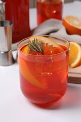 Aperol spritz cocktail, ice cubes, rosemary and orange slices in glass on white wooden table, closeup